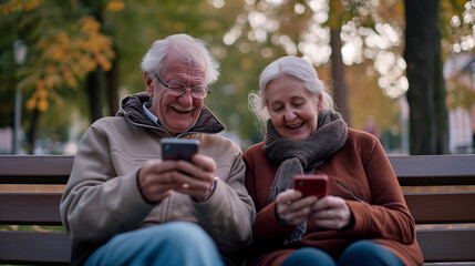An smiling elderly couple sits on a park bench, engrossed in their smartphones, smiling use their gadgets
