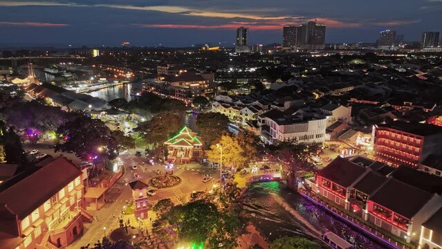 Aerial evening shot of Malacca city center, Melaka Tengah District, Malaysia. River with embankment, ancient colonial buildings with illumination in Malacca. Red sunset sky at background