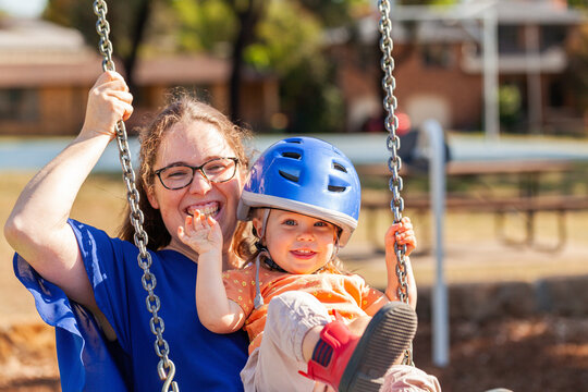 Mum with her little girl swinging together on swings at park