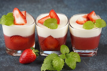 Vanilla panna cotta with strawberry layer in a small portioned vase and fruit pieces in wineglasses. Delicious Italian dessert.