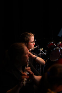 Flautist playing on musical instrument in back row of performers at music concert