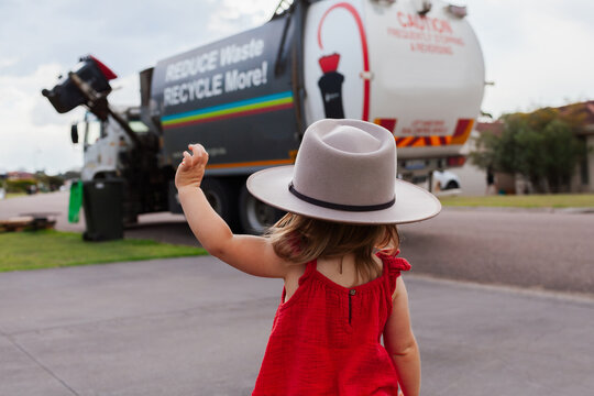 Litle aussie toddler outside waving to garbage truck man as he empties rubbish bins