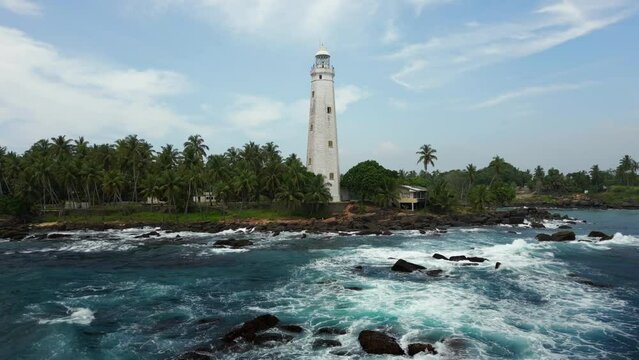 White colonial Dondra Head lighthouse surrounded by the stormy ocean, waves and palms on the jungle coast of Sri Lanka