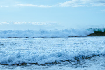 Panoramic sea view from the beach with splashing waves. Blue sky and horizon over ocean water in the background with the outline of an island
