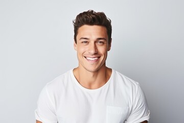 Handsome young man looking at camera and smiling while standing against grey background