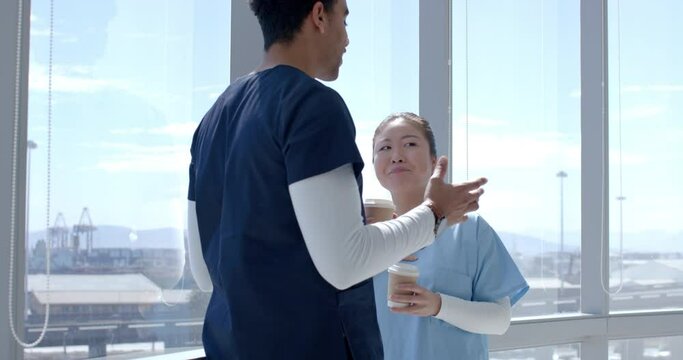 Young Asian healthcare worker and biracial healthcare worker converse in a bright hospital