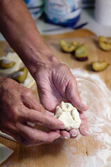 Preparation of homemade fruit dumplings with plums. Czech specialty of sweet good food. Dough on kitchen wooden table with hands.