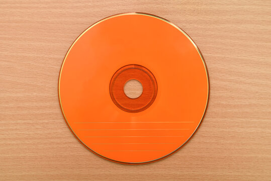 Orange CD or DVD on the brown wooden table. Vintage technology concept. Top view.