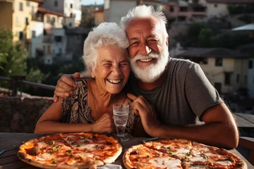 Fotobehang Happy senior old couple have fun eating a pizza together outdoor in traditional italian pizzeria restaurant sitting and talking and laughing. People enjoying food and elderly lifestyle. Retirement © simona
