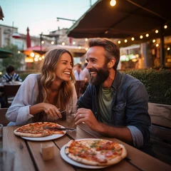 Wandaufkleber Happy young adult couple have fun eating a pizza together outdoor in traditional italian pizzeria restaurant sitting and talking and laughing. People enjoying food and dating relationship. Tourists © simona