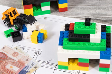 Houses made of toy blocks, miniature excavator, electrical diagrams of house and euro banknotes. Building home costs