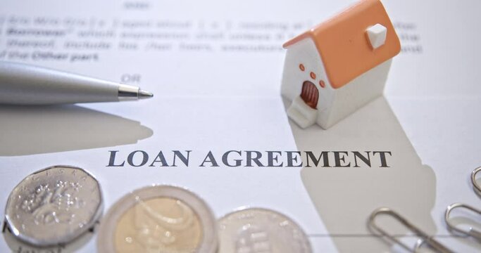 Mortgage loan or home equity loan, financial concept : A loan agreement form with a tiny model residential home, depicting home loan or borrowing money to purchase a new home for first time homebuyer.