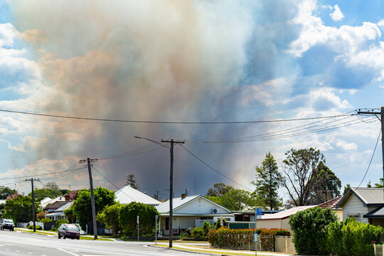 Bushfire smoke billowing into sky behind houses along main street of country town in Hunter Valley