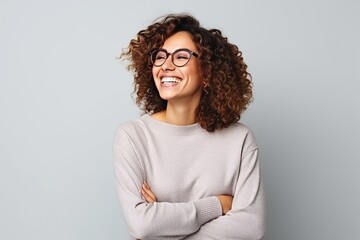 Portrait of a smiling young woman with curly hair and eyeglasses against grey background - Powered by Adobe