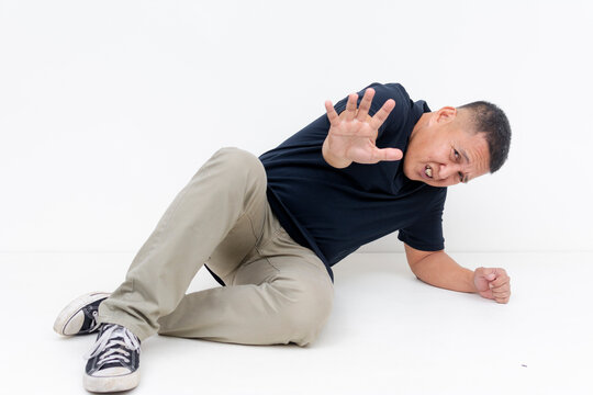 A scared middle aged Asian man drops on the ground showing fear with a defensive posture, begging not to be harmed.
