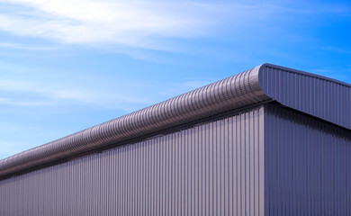 Curve corrugated metal roof eaves with gray aluminium steel wall of modern industrial rental warehouse building against blue sky background, low angle and perspective side view