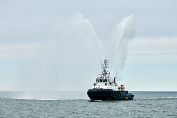 Fireboat ship sails on open sea directing jets of water to sides demonstrating bravery water...