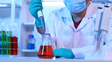 Scientists are doing research in a science lab. A medical chemist in a white coat, gloves and...