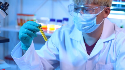 Scientists are doing research in a science lab. A medical chemist in a white coat, gloves and goggles looks at a glass tube. Compare two different liquid samples. and discuss future experiments.