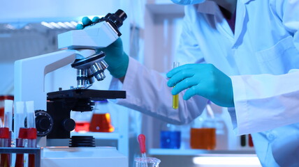 Scientists are doing research in a science lab. A medical chemist in a white coat, gloves and goggles looks at a glass tube. Compare two different liquid samples. and discuss future experiments.