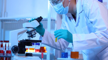 Scientists are doing research in a science lab. A medical chemist in a white coat, gloves and goggles looks at a glass tube. Compare two different liquid samples. and discuss future experiments. - obrazy, fototapety, plakaty