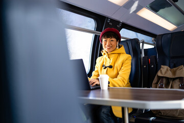 Beautiful woman traveling by train, working on laptop computer and enjoying the journey.
