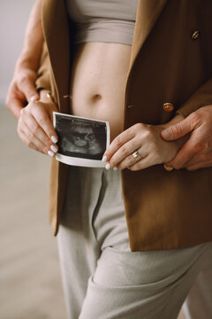 Pregnant woman with her husband holding ultrasound photo near pregnant belly
