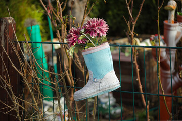 A rubber boot with flowers as a decoration on a garden fence