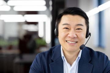 Professional Asian male in a blue suit with a headset smiling confidently in a corporate office...