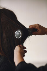 Close up of hairdressers hands drying long brunett  hair with blow dryer and round brush