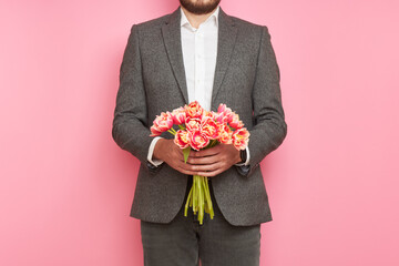 Romantic man in suit, with bouquet of tulips on isolated pink background, Valentine's Day, March 8