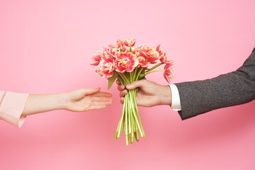 Couple in love holding a bouquet of tulips on a pink background. The concept of Valentine's Day, March 8
