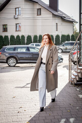 a beautiful woman with red hair in a gray coat walks through the city