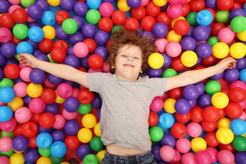 Fototapeta na wymiar Happy little boy lying on many colorful balls, top view