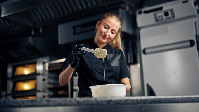 Girl chocolatier using a silicone spatula mixes chocolate for making desserts in pastry shop