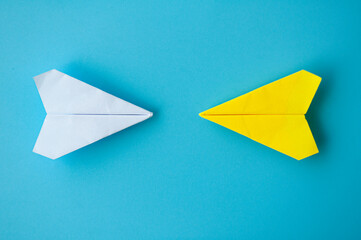 Top view of a white and yellow paper airplanes origami flying towards each other on blue background