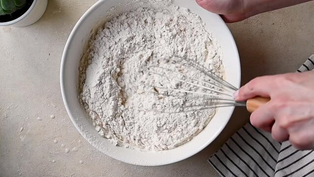 Female hands whisking flour dough batter in a bowl for pancakes or cake.