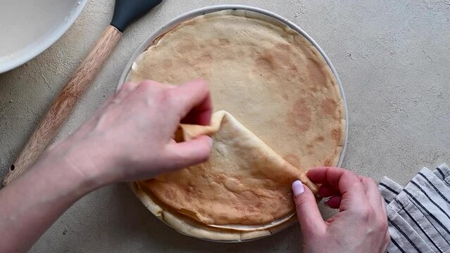 Female hands folding a thin crepe pancake, top view.