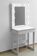 Modern white makeup dressing table with mirror and backlight on a white wall close-up.