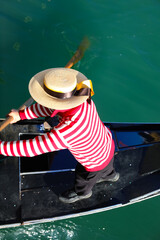 Venetian gondolier with hat rowing on gondola boat on the water of grand canal in Venice Italy