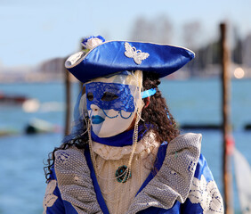 masked woman with blue hat and in the background the sea of Venice in Italy