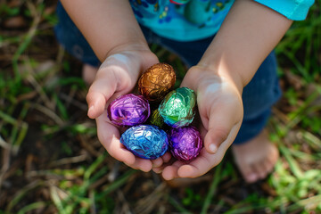 A child's hands are gently holding a cluster of vividly colored, foil-wrapped chocolate Easter eggs.