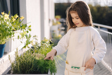 Four year old girl in bright overall stand by flowerpot and preparing to landing on balcony