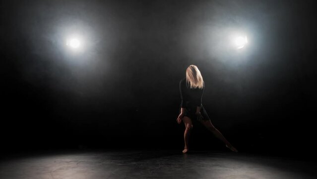 Woman choreographer dancing jumping. Blonde hard-working female ballerina dances in black dress in studio on stage. Performing dance element classical ballet bouncing in air. Practice choreography.