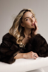 beautiful sexy woman with blond hair in luxurious fur coat posing in the studio