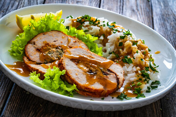 Stuffed turkey breast roulade with dried apricots and cranberries and boiled white rice on wooden table
