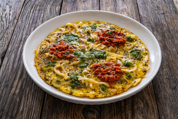 Tagliatelle omelet - scrambled eggs with mozzarella cheese, tagliatelle, basil and tomato pesto on wooden table
