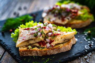 Tasty sandwiches - toasted bread with pickled herrings and red onion on wooden table
