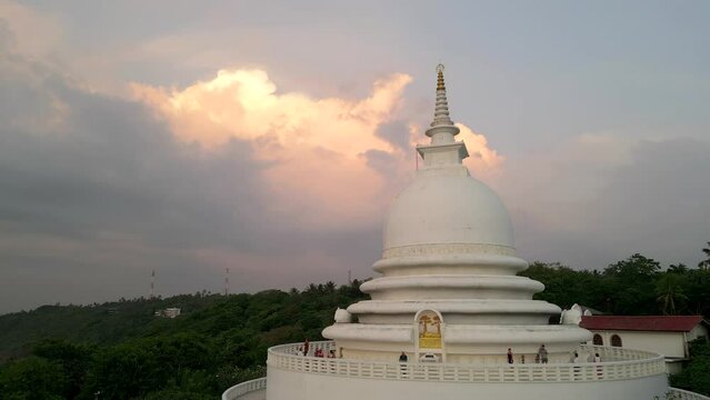 White pagoda buddhist temple among the jungle against the sunset clouds. Japanese Peace Pagoda in Sri Lanka aerial view.