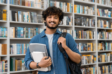 Portrait of cheerful international Indian student with backpack, learning accessories standing near...